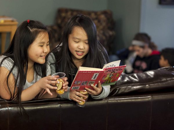 Kalena Vue, left, 9 3rd grade, and Angelina Vang, 10, 5th grade, have a snack and read at the Rolling Prairie Apartments in Sun Prairie in an after school program called the Homework Club March 17, 2015, in Sun Prairie. (Photo © Andy Manis)